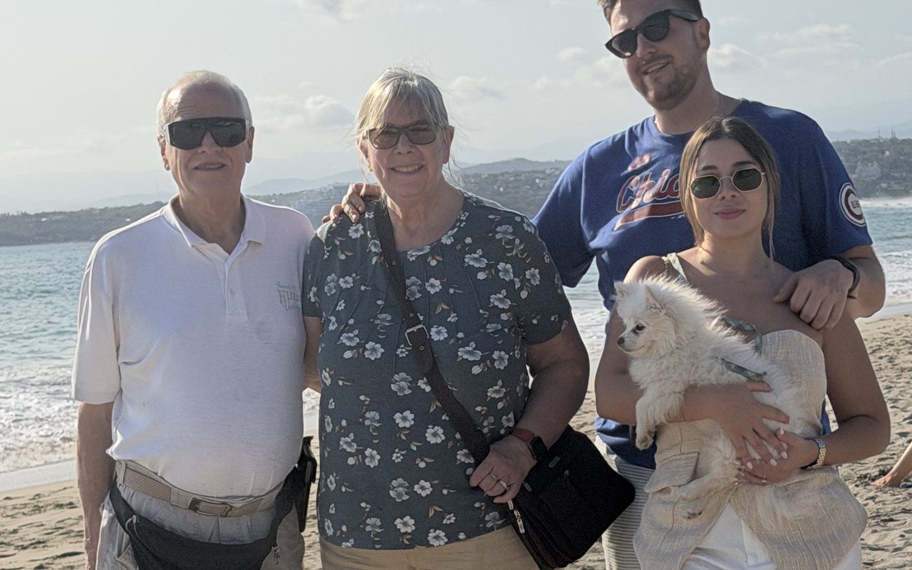 Andy with his mom and dad and his fiancée Carolina, who is holding a small white dog, on a beach